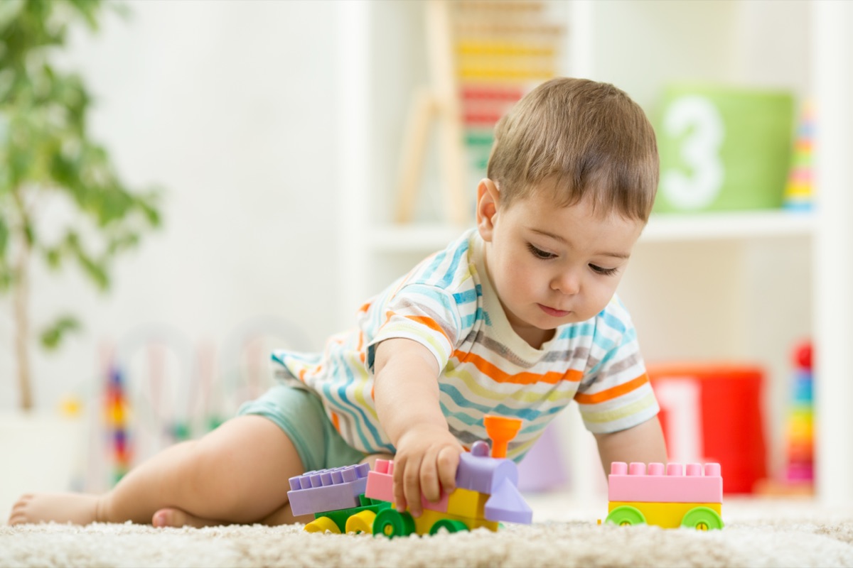 A baby crawling on a soft rug and playing with a colourful toy train